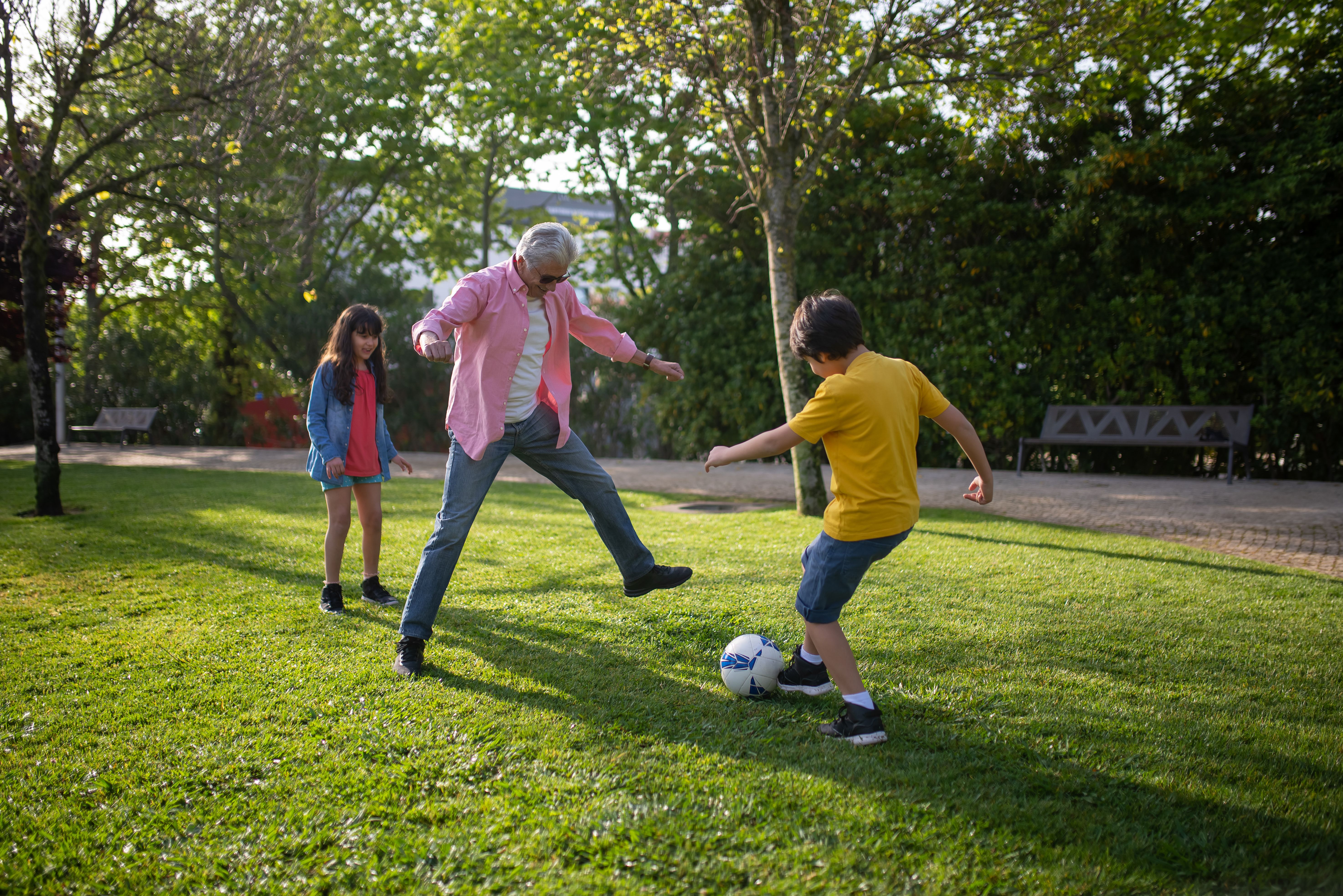 Una abuela juega al fútbol con sus nietos en un parque